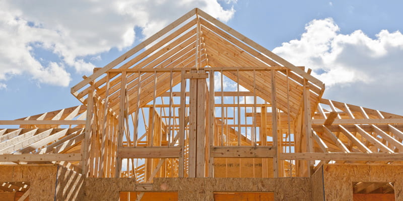 Wood framing of a residential house under construction against a blue sky with clouds