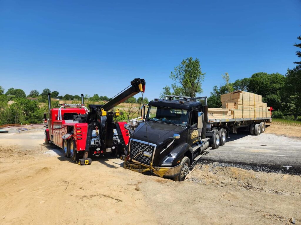 A heavy-duty wrecker lifting a heavily loaded lumber truck at a jobsite.