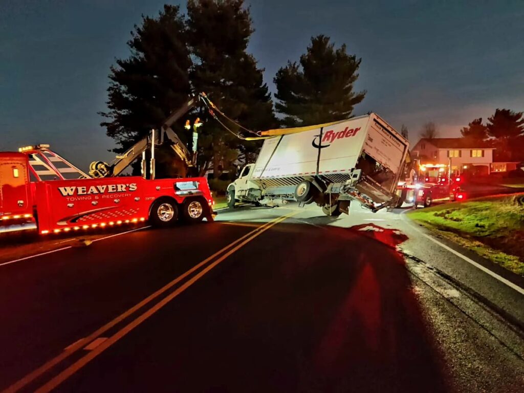 Weaver’s Towing wrecker lifting a Ryder box truck during a nighttime roadside recovery.