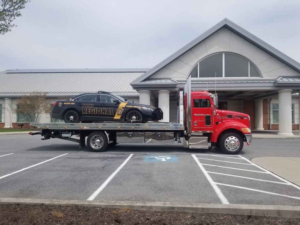 Weaver’s Towing rollback truck hauling a regional police car in a parking lot.