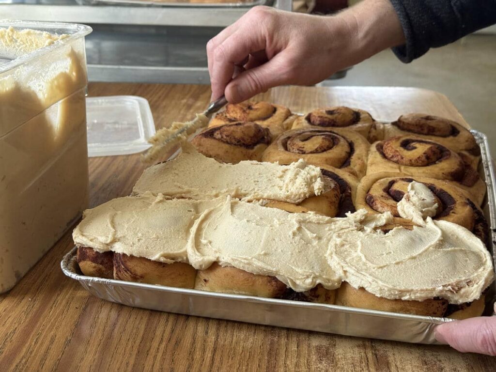 Icing being spread over fresh cinnamon rolls at Country Lane Bakery.